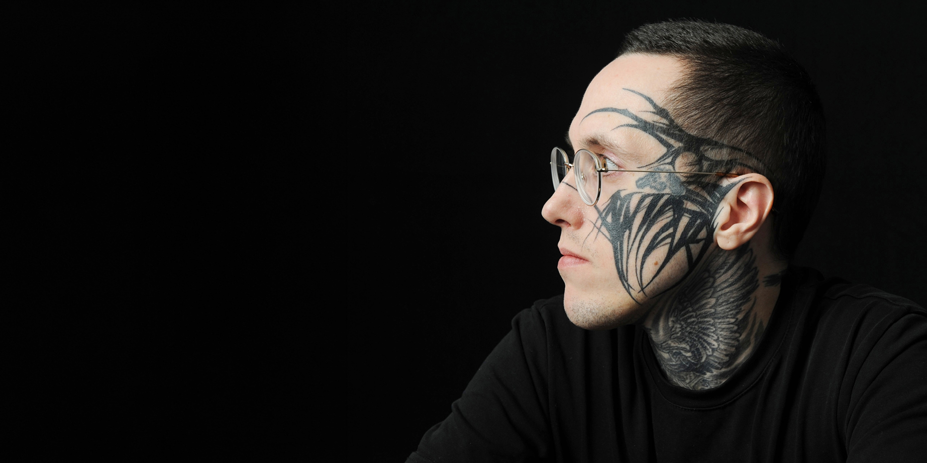 Profilporträt eines Mannes mit Tattoos und runder Brille aus dem Bildband Menschenbilder